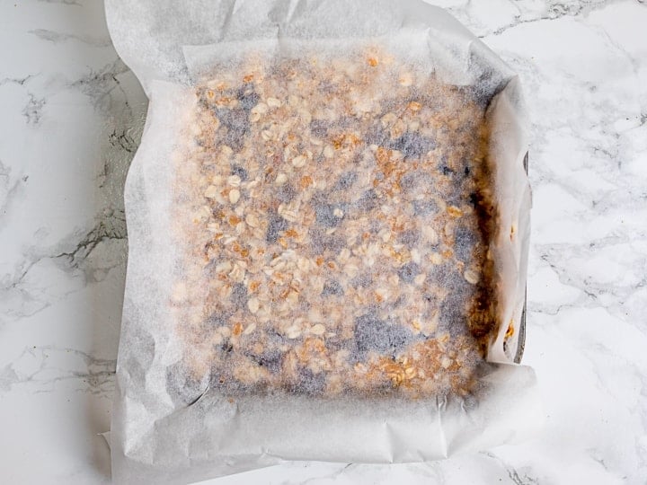 Granola bar mixture in a baking tin with baking parchment on top