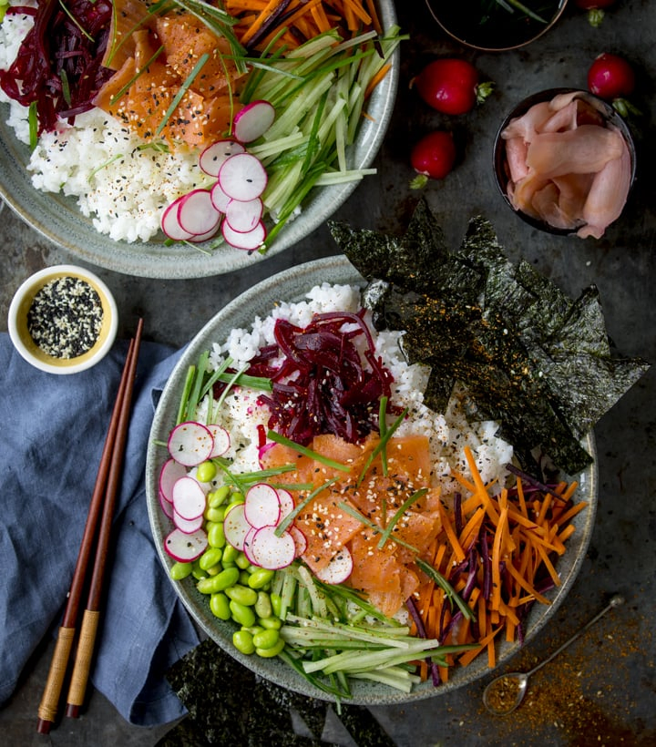 Overhead image of two deconstructed salmon sushi salad bowls on a dark background