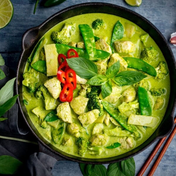A bowl of Thai Green Curry with chicken, broccoli, mangetout, bamboo shoots, red chilli slices, and fresh basil leaves in a fragrant Thai green curry sauce.