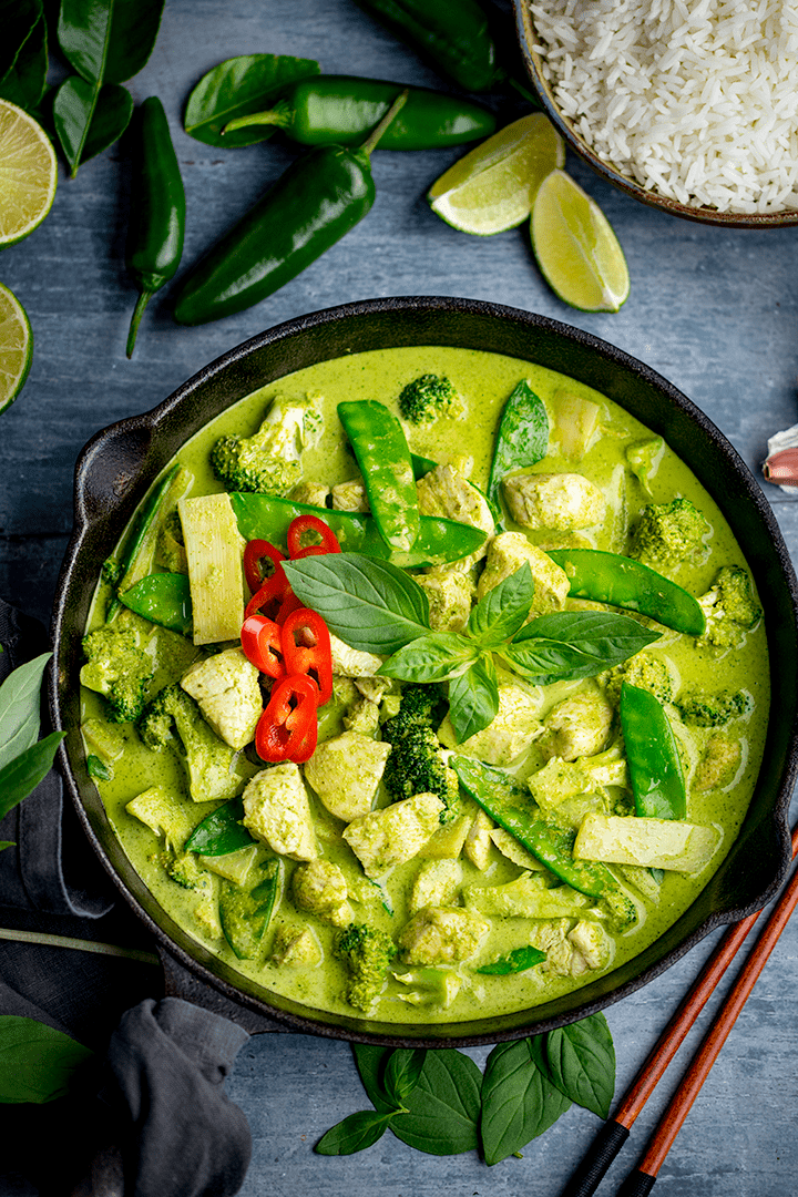 Tall image of a pan of Thai green chicken curry with vegetables on blue background