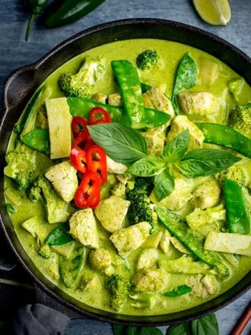 Square image of Pan of Thai green chicken curry with vegetables on blue background