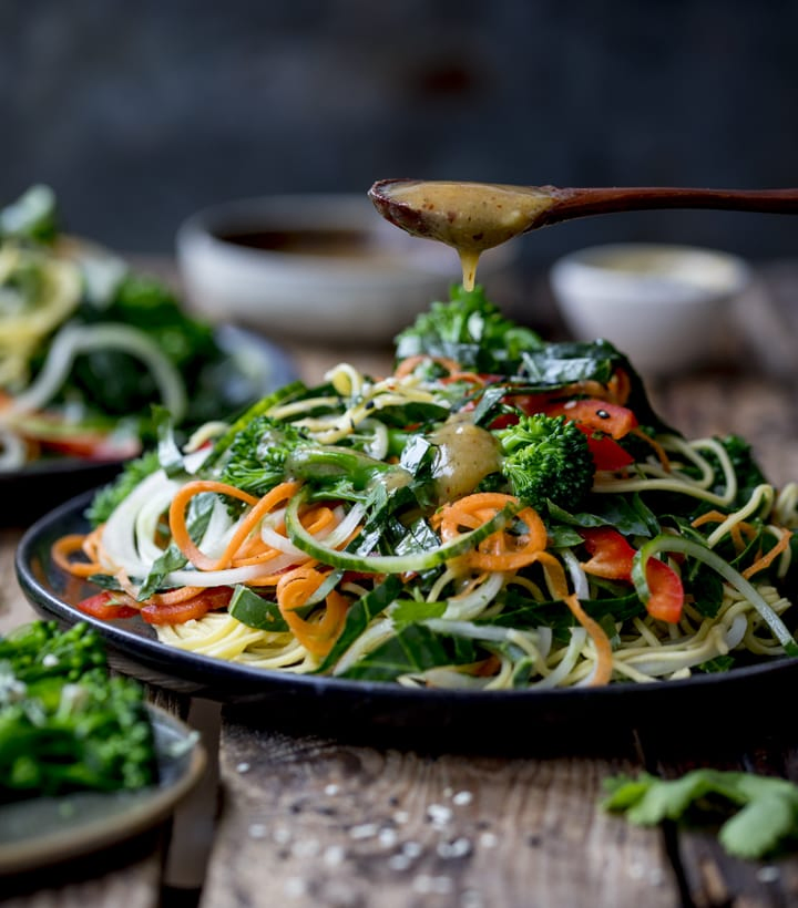 Side image of a winter noodle salad with salad dressing being dripped on from a spoon