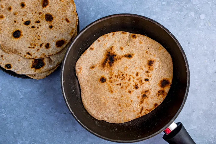 Chapati frying in a pan on a blue background