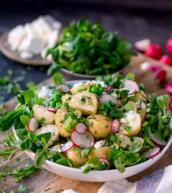 Green salad with new potatoes, radish slices and herb dressing in a white bowl
