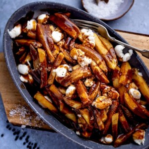 Poutine in a grey dish on a wooden board