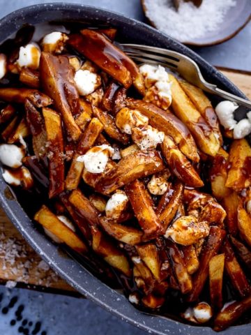 Poutine in a grey dish on a wooden board