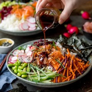 Pouring soy dressing on a sushi salmon bowl