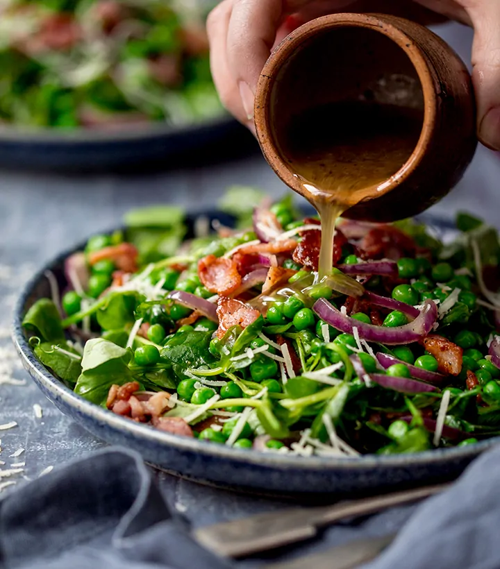 Dressing being poured onto a bacon and pea salad