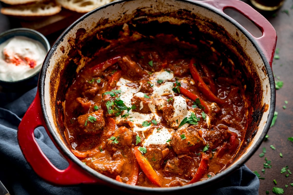 wide image of Beef Goulash in a red casserole pan, topped with sour cream
