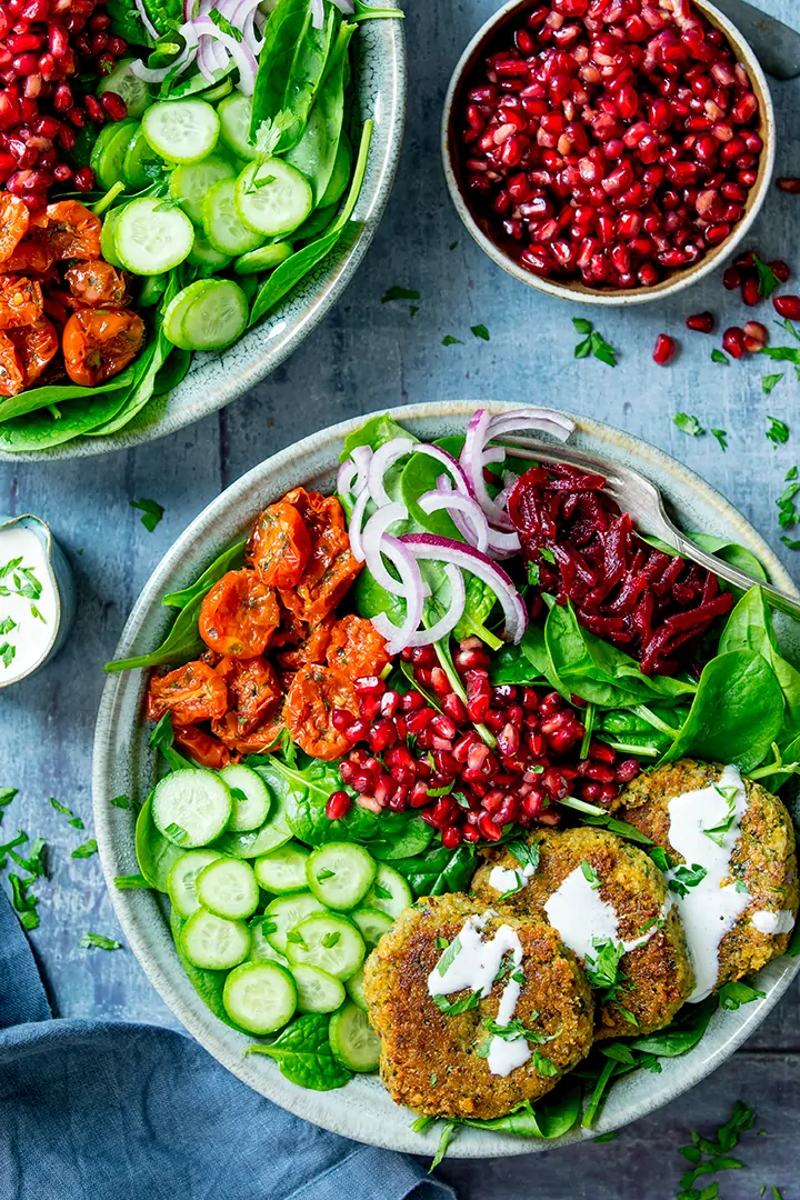 Two salad bowls with falafel and feta dressing on a blue background