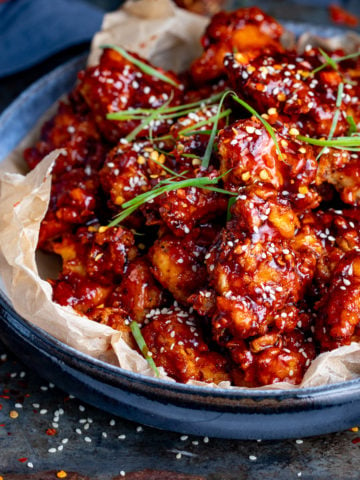 Bowl of Korean fried chicken topped with sesame seeds and strips of spring onion.