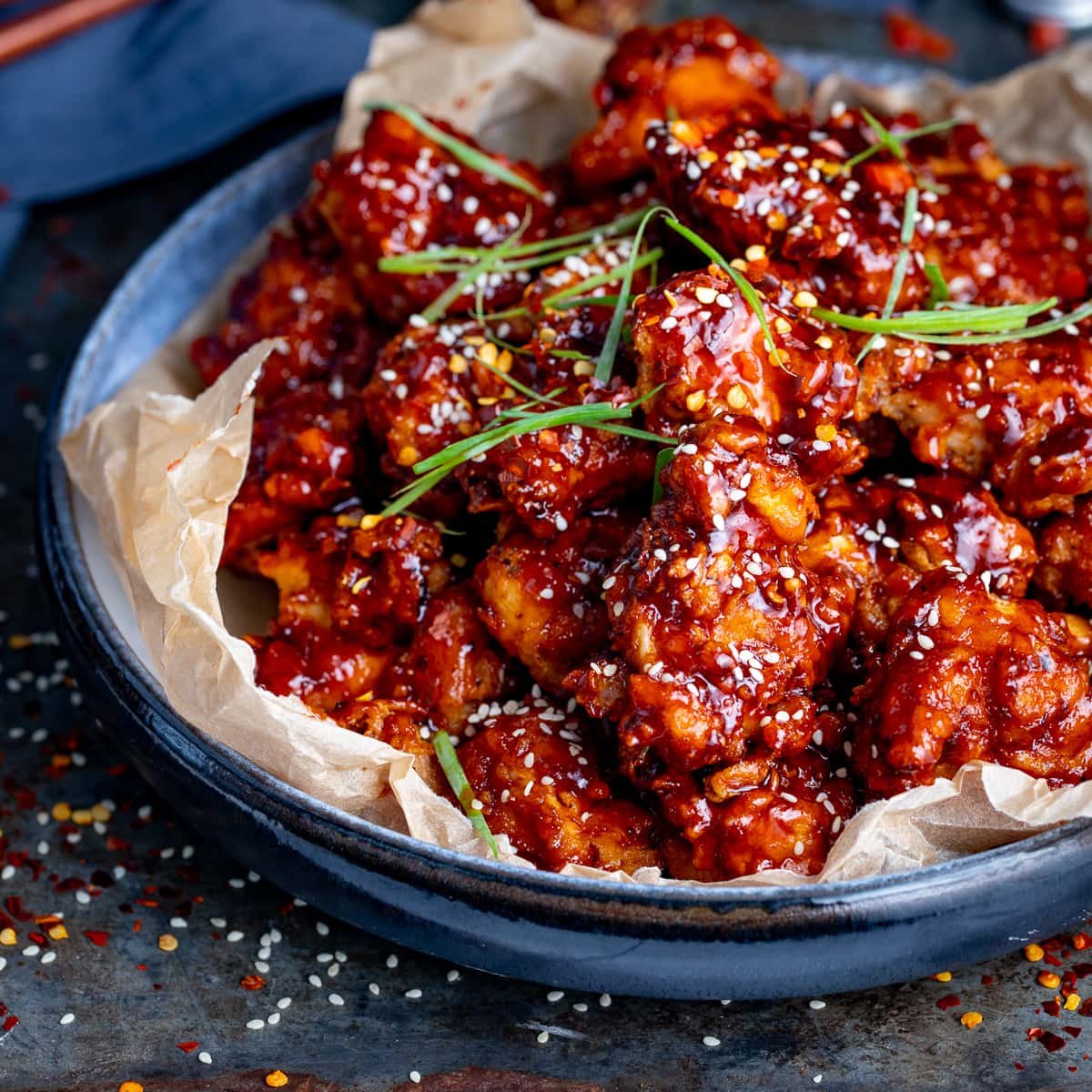 Bowl of Korean fried chicken topped with sesame seeds and strips of spring onion.