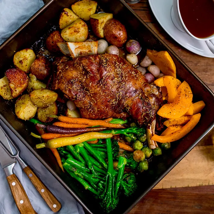 roast lamb shoulder and vegetables in a roasting tin with jug of gravy
