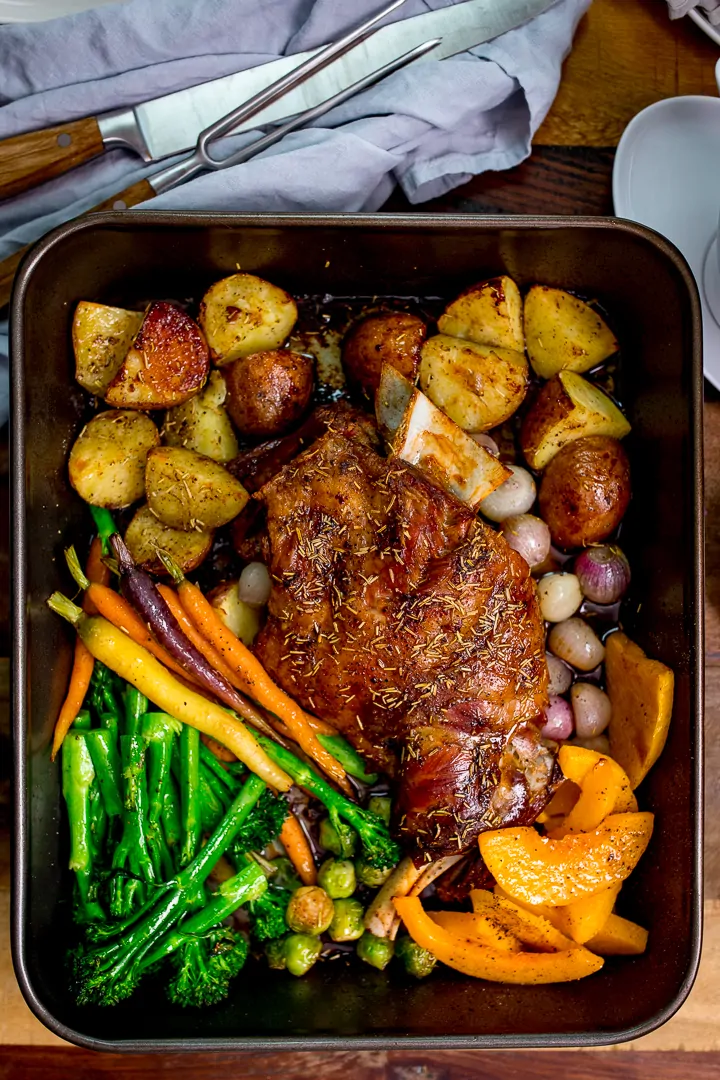 roast lamb shoulder and vegetables in a roasting tin with carving knife