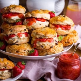 Piled up scones on a white cake stand with jar of rhubarb and strawberry compote