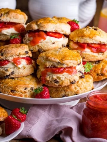 Piled up scones on a white cake stand with jar of rhubarb and strawberry compote