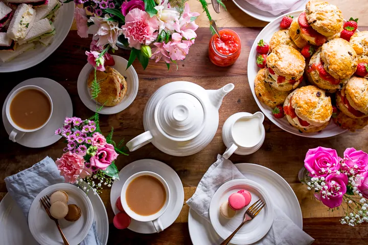 Overhead image of afternoon tea table with scones, flowers, tea and teapot on a wooden table.