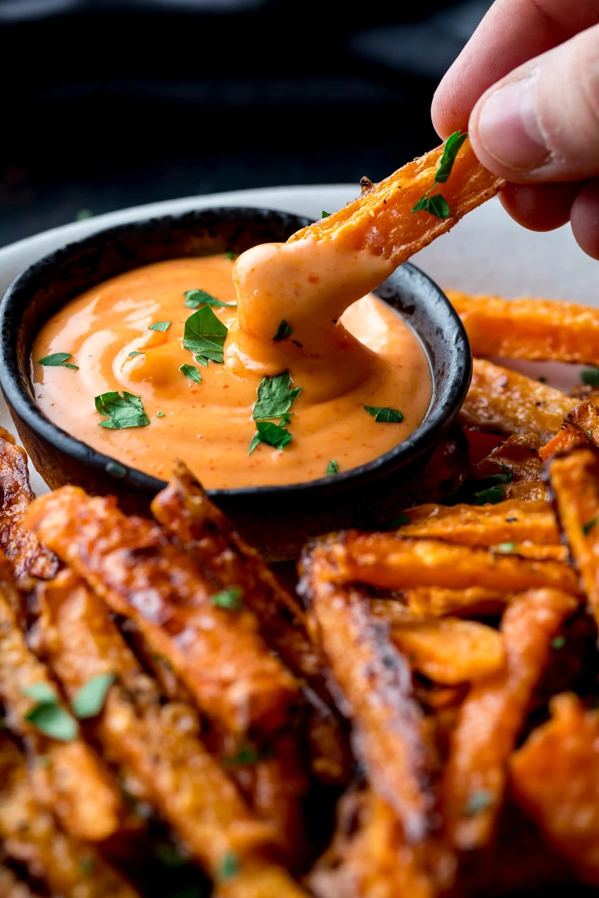 A carrot fry being dipped into sriracha mayo