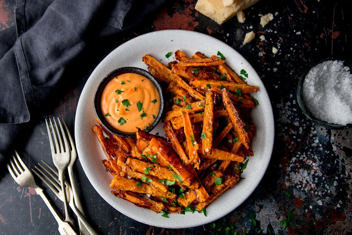 wide image of carrots fries and dip on a white plate with forks next to the plate