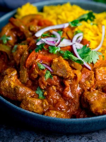 Close up image of chicken Jalfrezi with pilau rice in a blue bowl