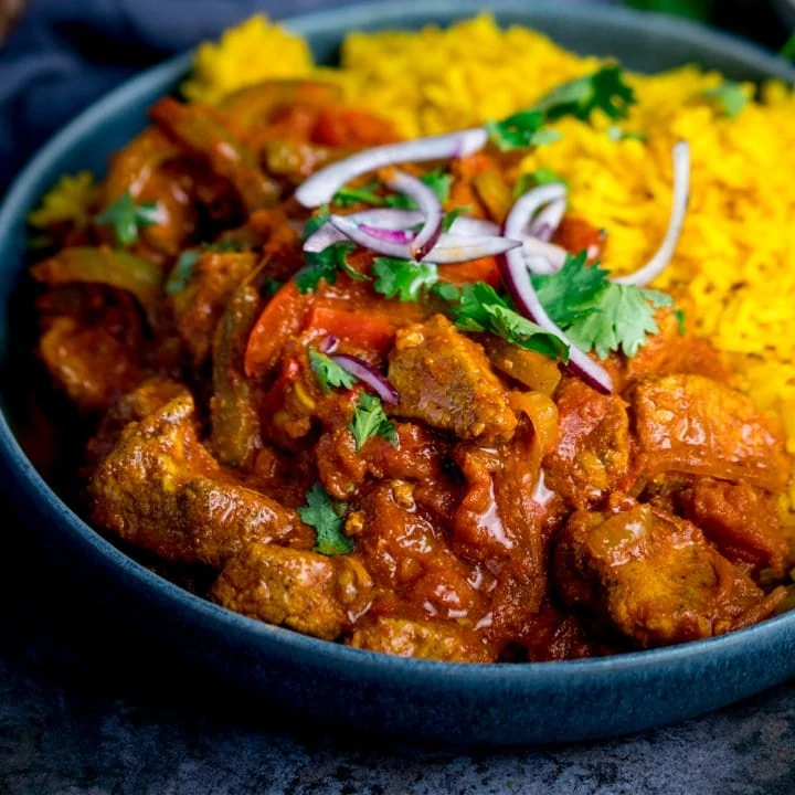 Close up image of chicken Jalfrezi with pilau rice in a blue bowl