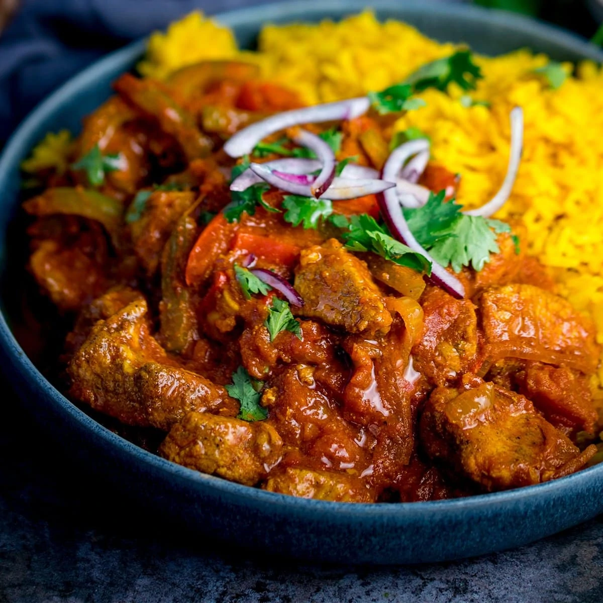 Close up image of chicken Jalfrezi with pilau rice in a blue bowl