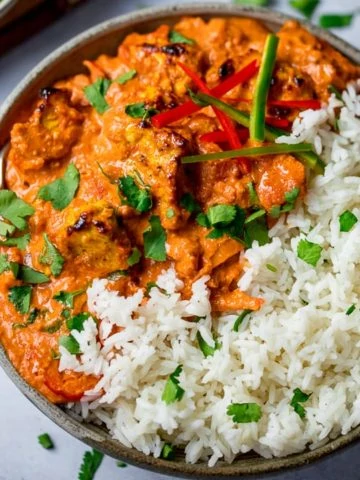 Bowl of chicken tikka masala with rice on a light background