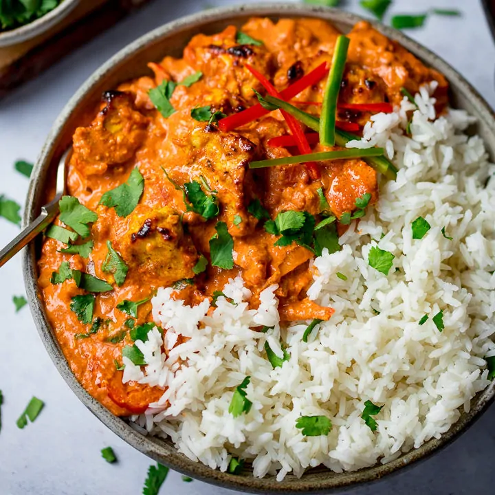 Bowl of chicken tikka masala with rice on a light background