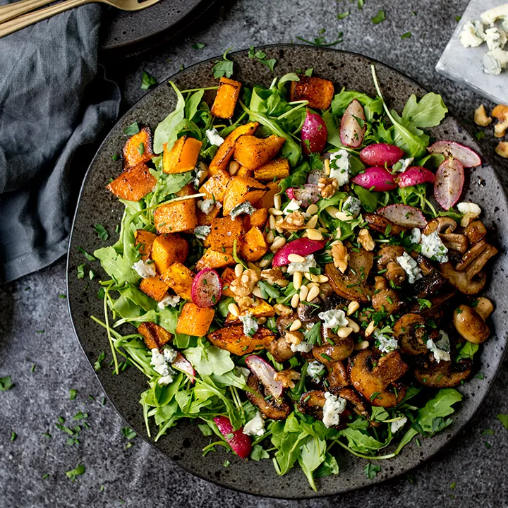 Garlic mushroom and roasted squash salad on a dark plate on a dark background