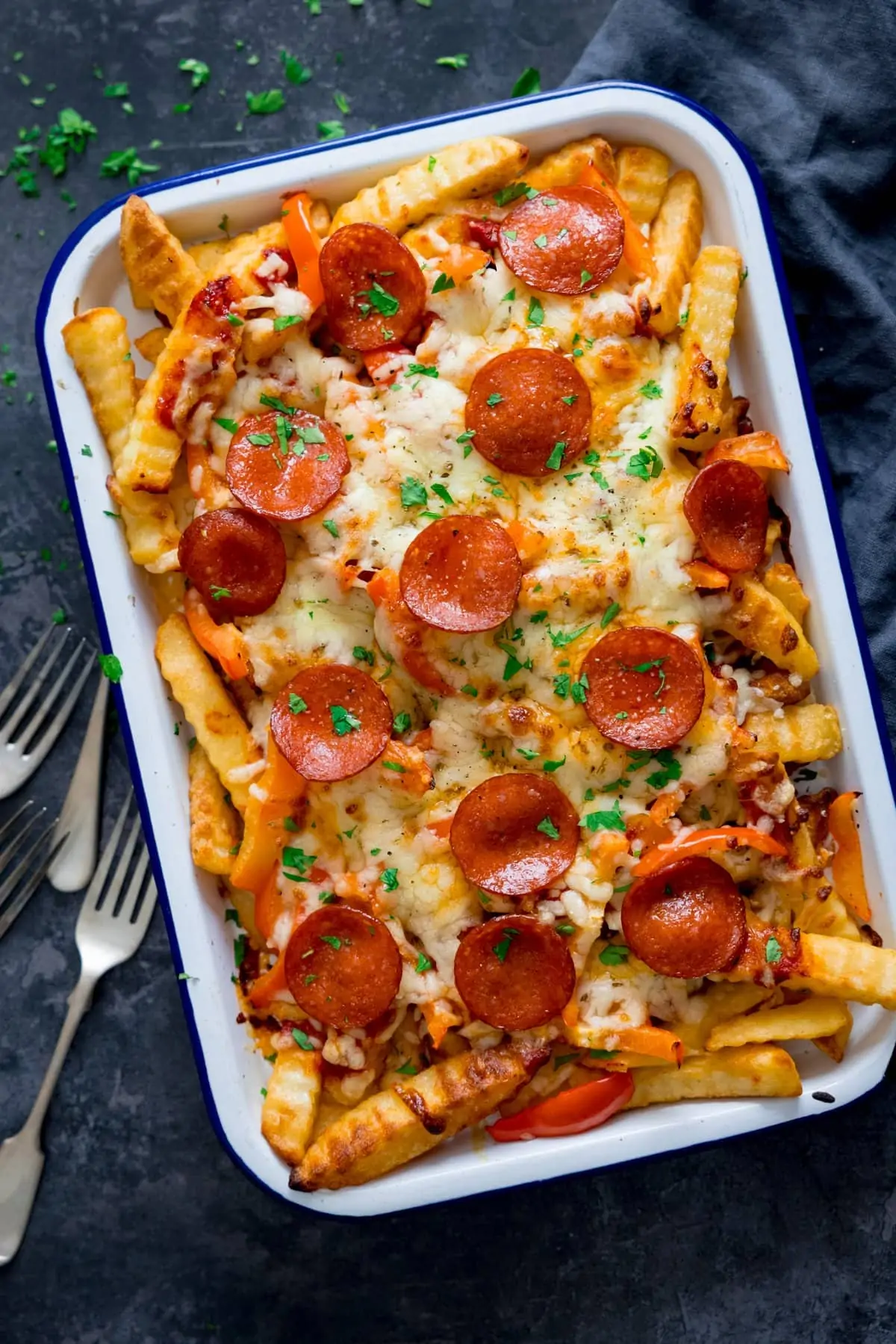 Overhead shot of pizza fries on a white tray on a dark background. Forks and a blue napkin are around the tray.