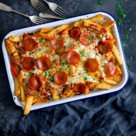 Square image of pizza fries on a white baking tray on a dark blue background with a blue napkin and forks around the tray.