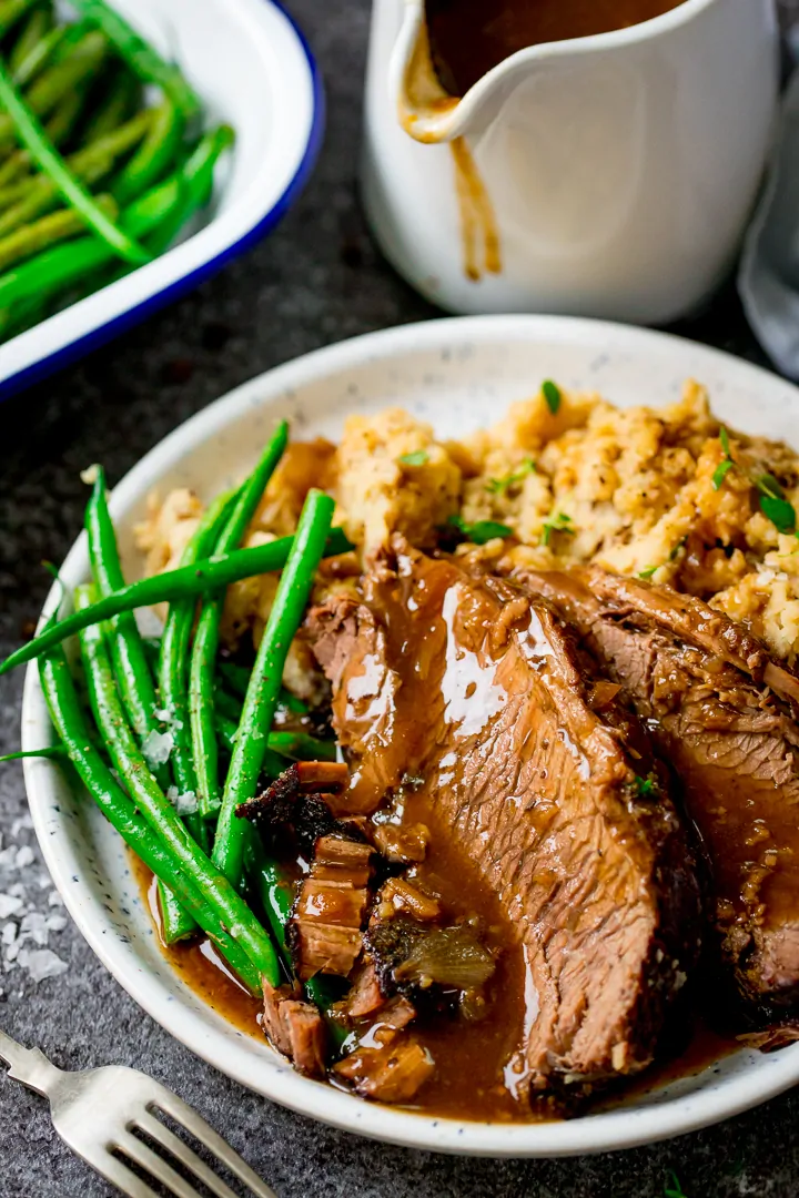 plate of sliced beef, vegetables and gravy with gravy jug in background