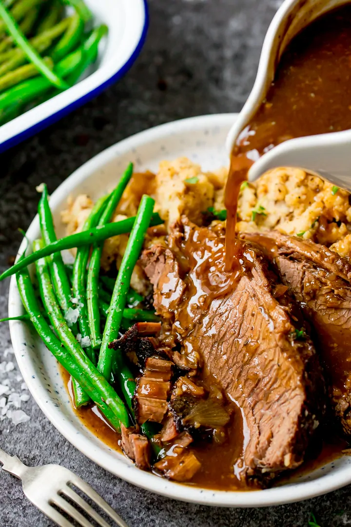 Gravy being poured onto plate of sliced beef and vegetables.