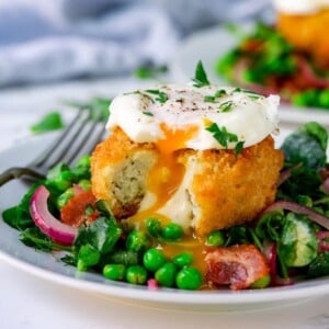 pea and bacon salad topped with a fish cake and poached egg that have been cut into.
