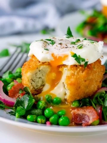 pea and bacon salad topped with a fish cake and poached egg that have been cut into.