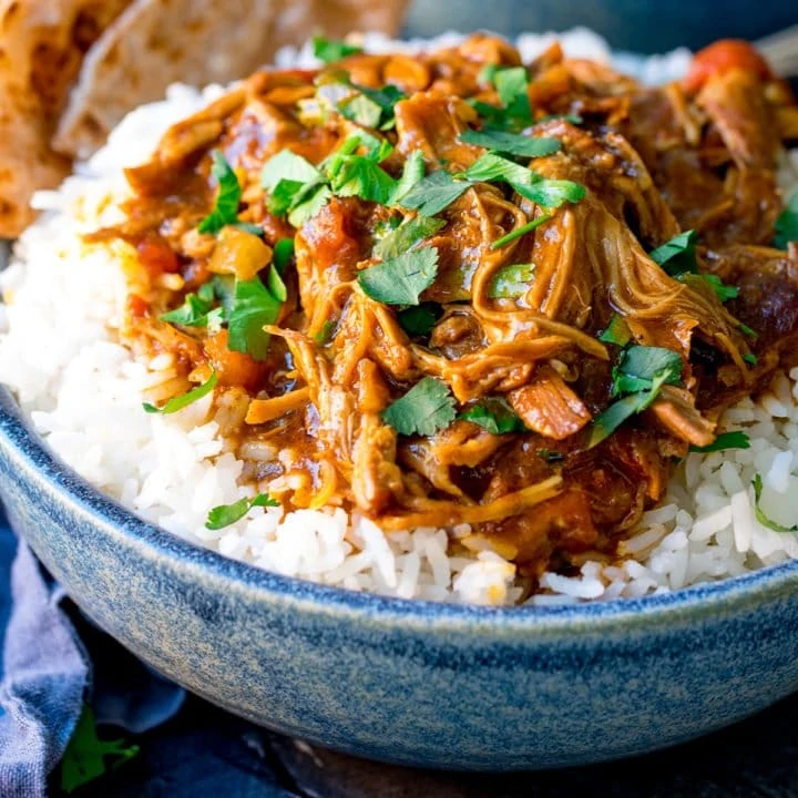 Close up picture of slow Cooked Pulled Lamb Curry on a bed of boiled rice in a blue bowl