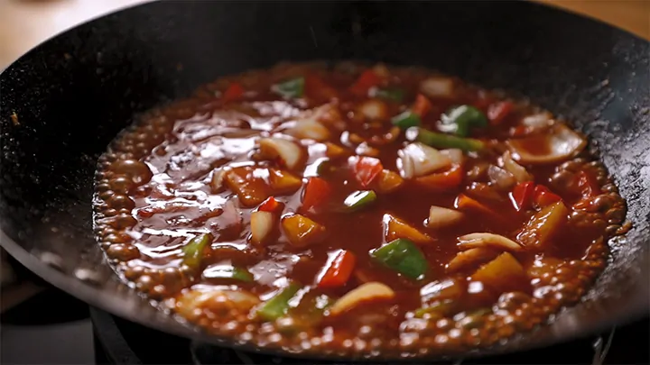 Sweet and sour sauce with vegetables bubbling in a wok