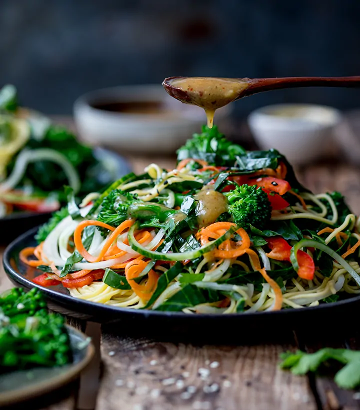 miso dressing being drizzled onto a noodle salad on a wooden background