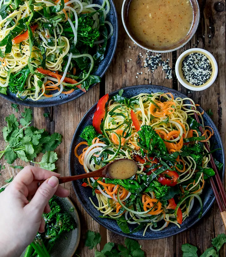 Overhead image of miso dressing being drizzled on a noodle salad on a dark background