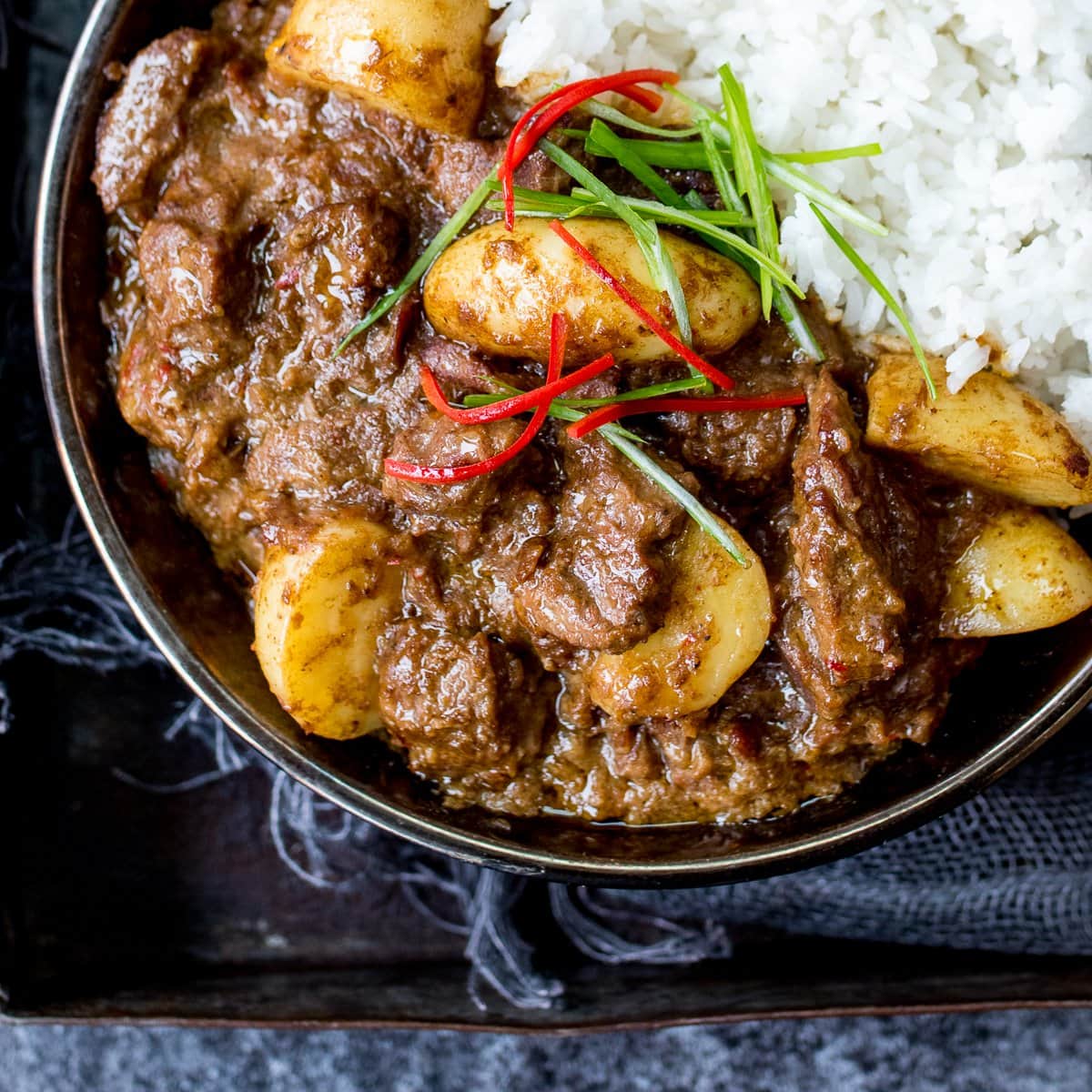 A bowl of beef massaman curry with rice on a dark background