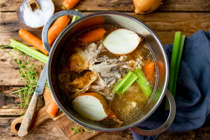 Overhead shot of pan filled with chicken stock ingredients on a wooden board