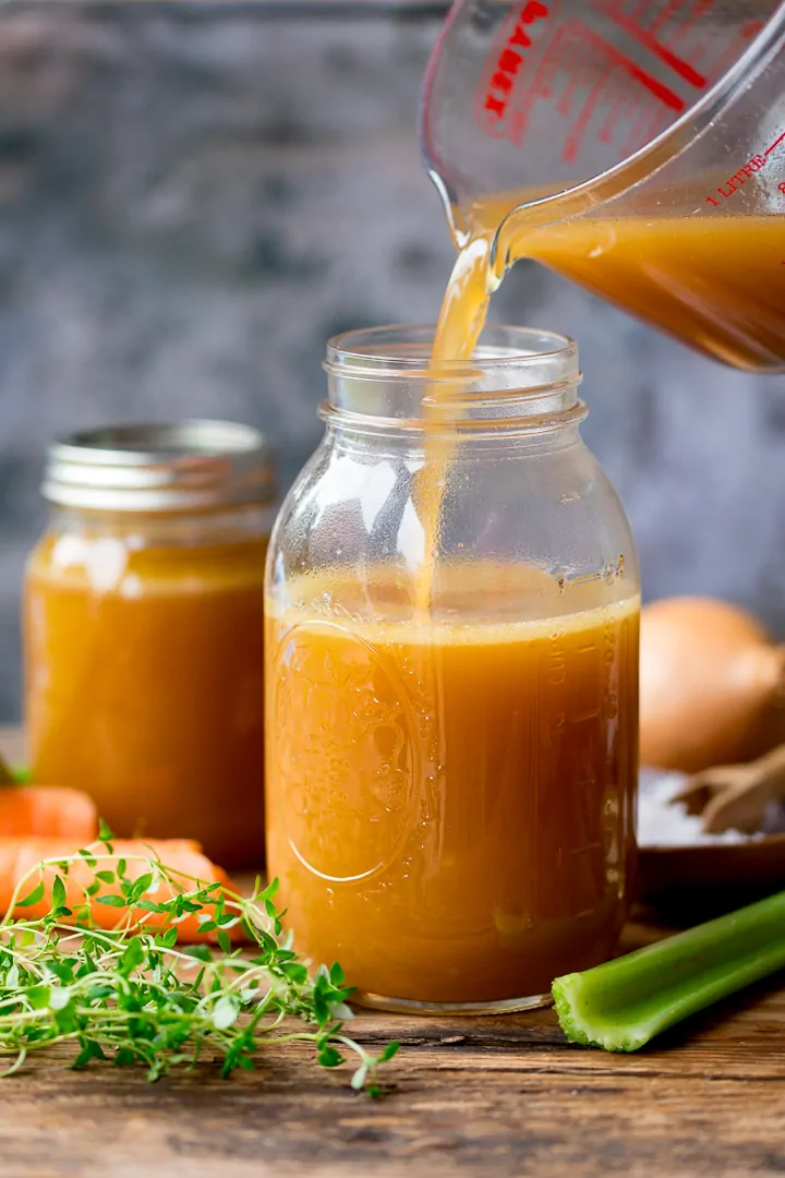 Chicken stock being poured in a glass mason jar