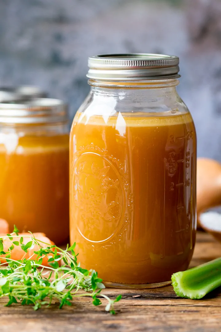 Glass mason jar filled with chicken stock on a wooden board