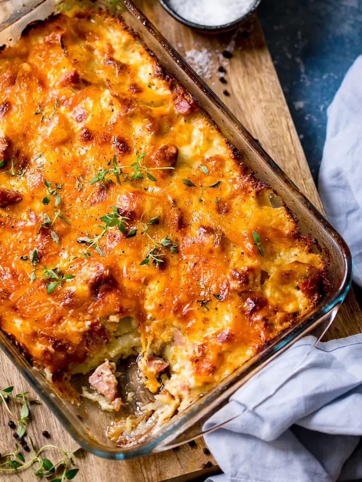 Scalloped potatoes with ham in a dish on a wooden board