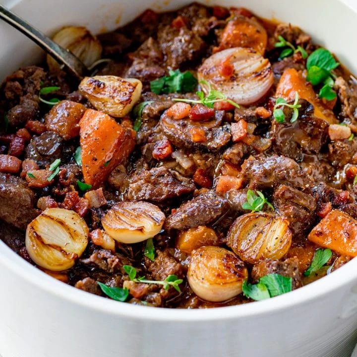 Close up view of beef bourguignon in a pot with a rustic spoon sticking out of it