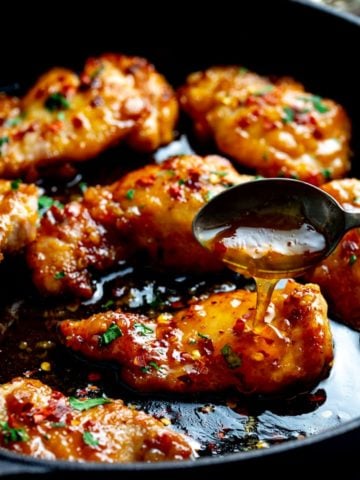 honey garlic chicken in a dark pan with sauce being spooned over