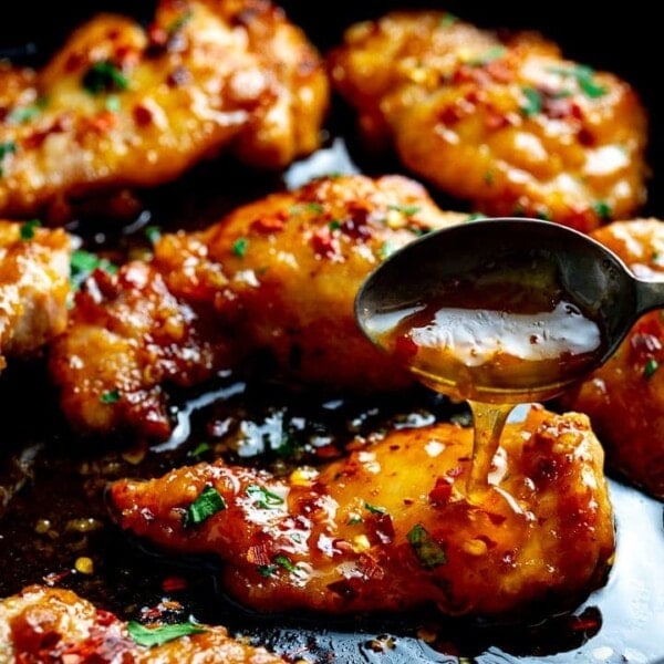 honey garlic chicken in a dark pan with sauce being spooned over