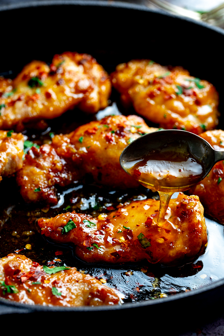 honey garlic chicken in a dark pan with sauce being spooned over