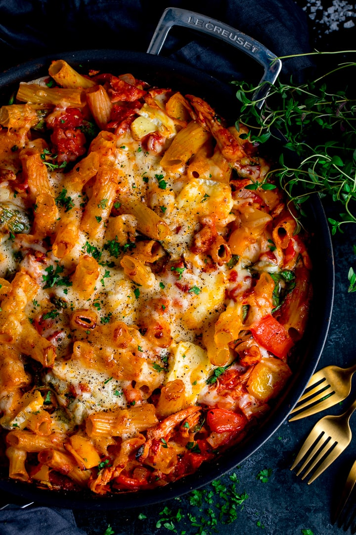 Leftover turkey, ham and cheese pasta bake in a black pan on dark background with gold forks in shot