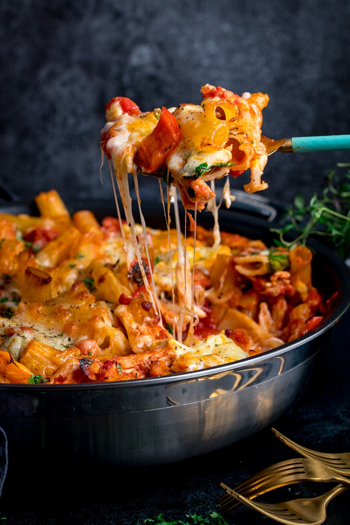 Side shot of Leftover turkey, ham and cheese pasta bake in a black pan with a scoop being lifted out